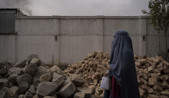 A woman passes a pile of bricks that will be used for the construction of a mosque in the Mirbacha Kot hospital, Afghanistan on Tuesday, Oct. 26, 2021. The construction of the mosque is the new manager&#x27;s top priority as health care workers continue to work without salaries, without medicine and with frequent power cuts in Afghanistan&#x27;s crumbling economy. (AP Photo/Bram Janssen)