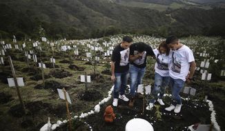 Relatives of Luis Enrique Rodriguez, who died of COVID-19, visit where he was buried on a hill at the El Pajonal de Cogua Natural Reserve, in Cogua, north of Bogota, Colombia, Monday, Oct. 25, 2021. Rodriguez died May 14, 2021. Relatives bury the ashes of their loved ones who died of coronavirus and plant a tree in their memory. (AP Photo/Ivan Valencia)