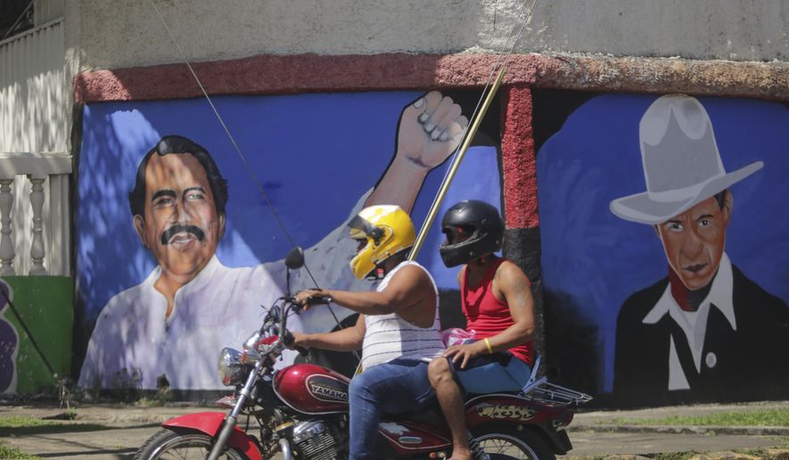 A motorcyclist rides past a mural of Nicaraguan President Daniel Ortega, left, and revolutionary hero Cesar Augusto Sandino during general elections in Managua, Nicaragua, Sunday, Nov. 7, 2021. Ortega seeks a fourth consecutive term against a field of little-known candidates while those who could have given him a real challenge sit in jail. (AP Photo/Andres Nunes)