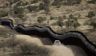 In this March 2, 2019, file photo, a Customs and Border Control agent patrols on the U.S. side of a razor-wire-covered border wall along Mexico east of Nogales, Ariz. (AP Photo/Charlie Riedel, File)