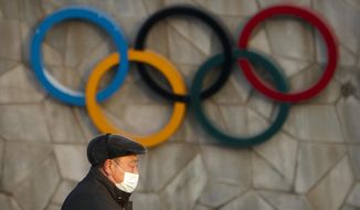 A man walks past the Olympic rings on the exterior of the National Stadium, also known as the Bird&#39;s Nest, which will be a venue for the upcoming 2022 Winter Olympics, in Beijing, Tuesday, Feb. 2, 2021. Making an Olympic team is hard enough. This winter, those who earn their spots on the U.S. squad will find it takes even more work to get to Beijing. (AP Photo/Mark Schiefelbein, File)