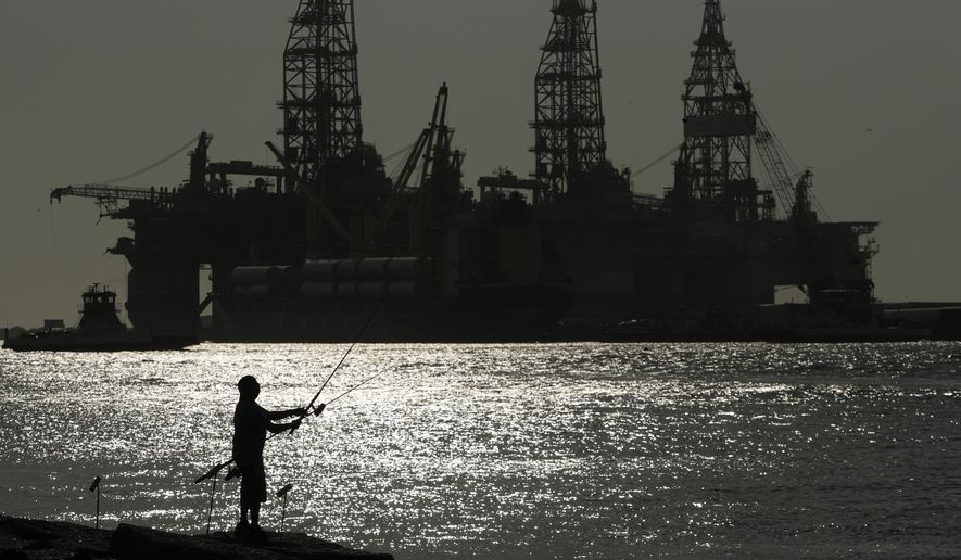 A man wears a face mark as he fishes near docked oil drilling platforms, Friday, May 8, 2020, in Port Aransas, Texas. (AP Photo/Eric Gay, File)