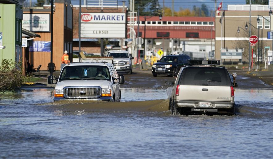 Cars drive through floodwaters Wednesday, Nov. 17, 2021, in Sumas, Wash. People in the small city of Sumas are assessing damage from flooding that hit an estimated three quarters of homes in the community near the Canadian border. (AP Photo/Elaine Thompson)