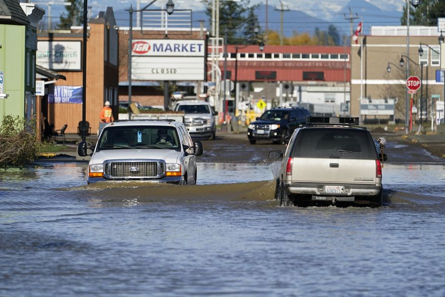 Cars drive through floodwaters Wednesday, Nov. 17, 2021, in Sumas, Wash. People in the small city of Sumas are assessing damage from flooding that hit an estimated three quarters of homes in the community near the Canadian border. (AP Photo/Elaine Thompson)