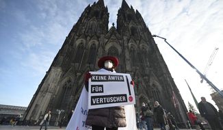 A participant of a rally of the initiative Maria 2.0 holds a poster with the inscription &#39;No offices for cover-ups&#39; in front of the cathedral in Cologne, Germany, Thursday, Nov. 18, 2021 before the beginning of a penitential service of the archdiocese of Cologne in the course of coming to terms with sexual violence.  (Henning Kaiser/dpa via AP)