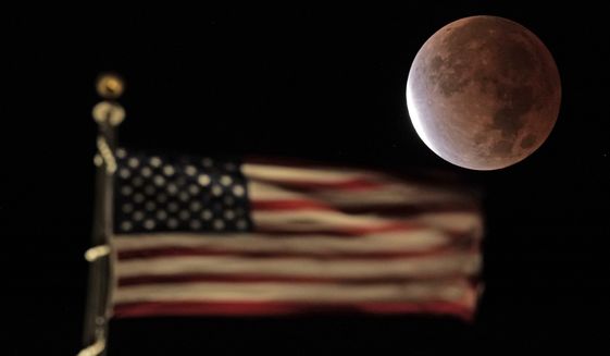 The earth&#39;s shadow covers the full moon during a partial lunar eclipse as it sets beyond the U.S. flag on top of a building, Friday, Nov. 19, 2021, in downtown Kansas City, Mo. (AP Photo/Charlie Riedel)