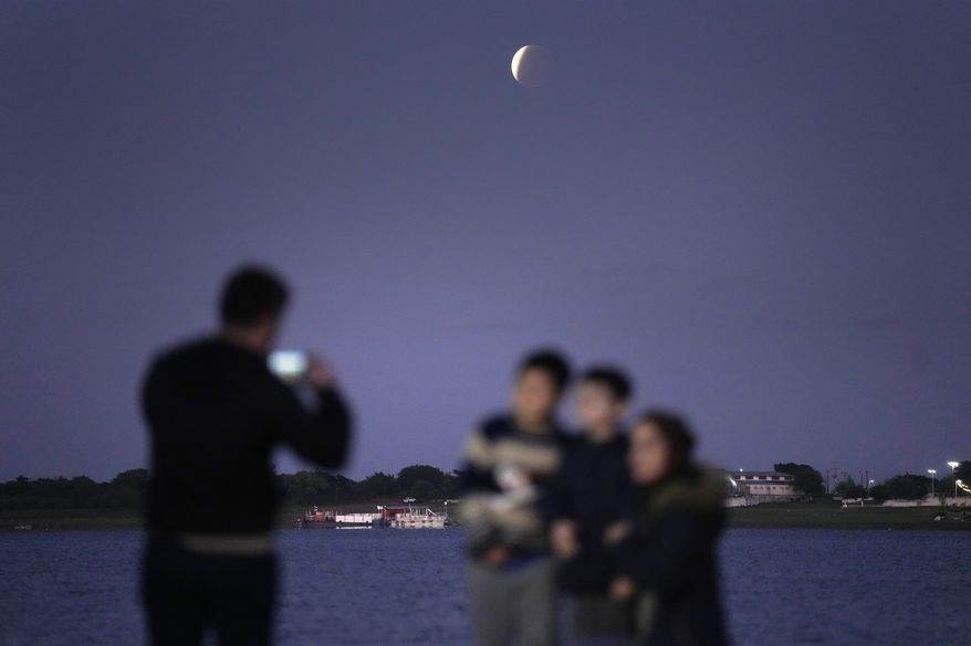Members of Prieto Yegros family take pictures as they watch the moon in partial eclipse in Asuncion's Bay, Paraguay, early Friday, Nov. 19, 2021. (AP Photo/Jorge Saenz)