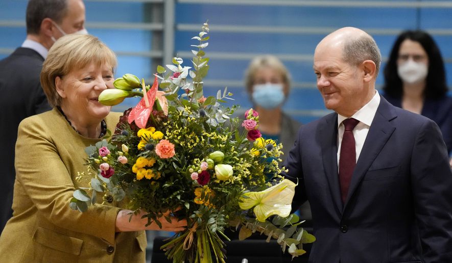 German Chancellor Angela Merkel (left) receives a bouquet from Vice Chancellor and Finance Minister Olaf Scholz (right) prior to the cabinet meeting at the chancellery in Berlin, Germany, Wednesday, Nov. 24, 2021. Merkel was given flowers as this was probably her last cabinet session as German chancellor as negotiations are going on to form a new government after elections were held in September. (AP Photo/Markus Schreiber, Pool)