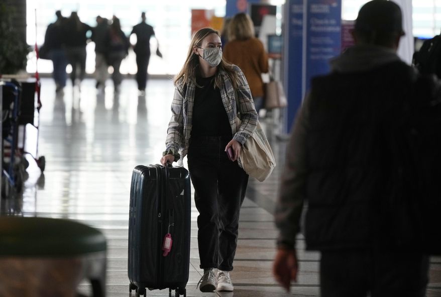 A traveller wears a face covering while heading to the American Airlines check-in counter as the Thanksgiving Day holiday approaches Tuesday, Nov. 23, 2021, at Denver International Airport in Denver. Wintry weather combined with the pandemic to frustrate air travelers whose return flights home from the holidays were canceled or delayed in the first days of the new year. (AP Photo/David Zalubowski)
