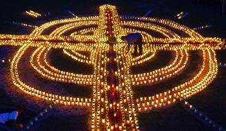 FILE - A woman lights candles forming a giant cross in memory of coronavirus victims in Germany in Zella-Mehlis, Germany, April 17, 2020. Germany is set to mark 100,000 deaths from COVID-19 this week, passing a somber milestone that several of its neighbors crossed months ago but which some in Western Europe&#x27;s most populous nation had hoped to avoid. (AP Photo/Jens Meyer, File)