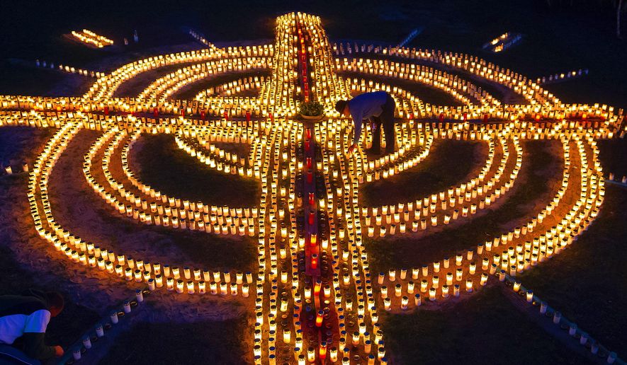 FILE - A woman lights candles forming a giant cross in memory of coronavirus victims in Germany in Zella-Mehlis, Germany, April 17, 2020. Germany is set to mark 100,000 deaths from COVID-19 this week, passing a somber milestone that several of its neighbors crossed months ago but which some in Western Europe&#39;s most populous nation had hoped to avoid. (AP Photo/Jens Meyer, File)