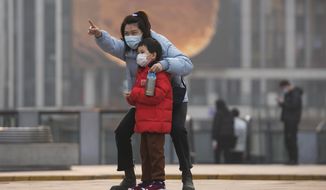 A woman and a child, both wearing face masks to protect from COVID-19 look at a commercial office building in Beijing, Sunday, Nov. 28, 2021. (AP Photo/Andy Wong)