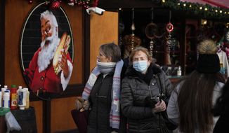 People walk past an image of Santa on the side of a stall in a Christmas market, in Trafalgar Square, London, Monday, Nov. 29, 2021. Countries around the world slammed their doors shut again to try to keep the new omicron variant at bay Monday, even as more cases of the mutant coronavirus emerged and scientists raced to figure out just how dangerous it might be. In Britain, mask-wearing in shops and on public transport will be required, starting Tuesday. (AP Photo/Matt Dunham)