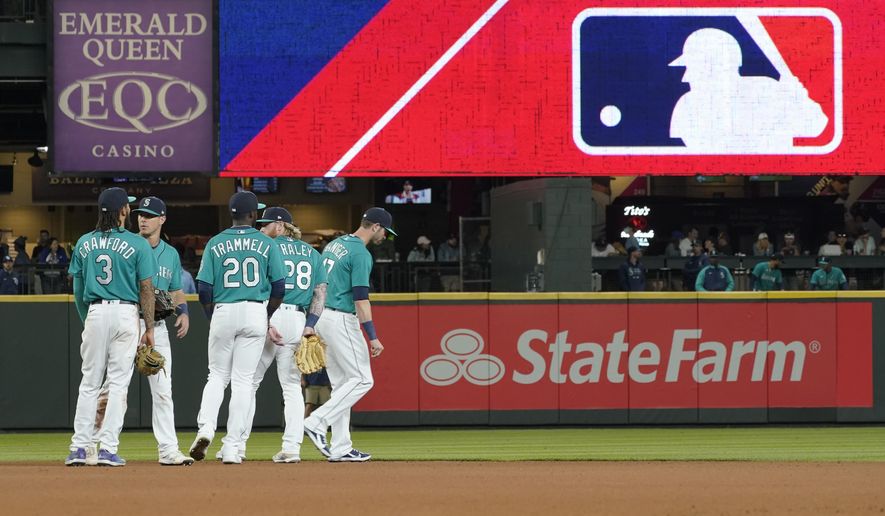 Seattle Mariners gather as the MLB logo is shown during a review of an attempted catch by right fielder Mitch Haniger of a ball hit by Tampa Bay Rays&#39; Ji-Man Choi that was originally called an out during the ninth inning of a baseball game Friday, June 18, 2021, in Seattle. The call was overturned. The Mariners won 5-1. The clock ticked down toward the expiration of Major League Baseball’s collective bargaining agreement at 11:59 p.m. EST Wednesday night, Dec. 1, 2021, and what was likely to be a management lockout ending the sport’s labor peace at over 26 1/2 years. (AP Photo/Ted S. Warren) **FILE**