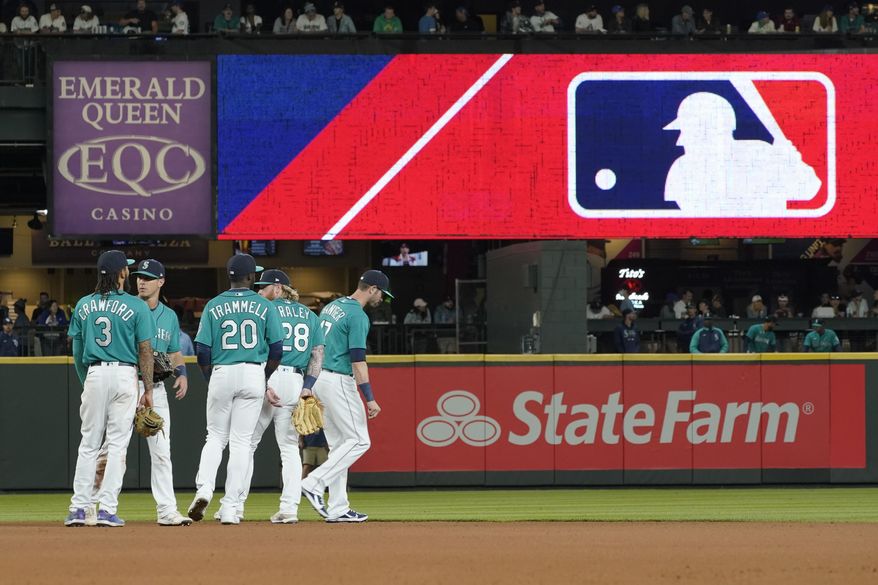 Seattle Mariners gather as the MLB logo is shown during a review of an attempted catch by right fielder Mitch Haniger of a ball hit by Tampa Bay Rays&#39; Ji-Man Choi that was originally called an out during the ninth inning of a baseball game Friday, June 18, 2021, in Seattle. The call was overturned. The Mariners won 5-1. The clock ticked down toward the expiration of Major League Baseball’s collective bargaining agreement at 11:59 p.m. EST Wednesday night, Dec. 1, 2021, and what was likely to be a management lockout ending the sport’s labor peace at over 26 1/2 years. (AP Photo/Ted S. Warren) **FILE**