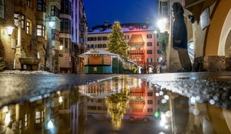 FILE - The Christmas tree of the closed Christmas market is reflected in a puddle in Innsbruck, Austria, Monday, Nov. 29, 2021. As countries shut their doors to foreign tourists or reimpose restrictions because of the new omicron variant of the coronavirus, tourism that was just finding it&#39;s footing again could face another major pandemic slowdown amid the uncertainty about the new strain. (Photo/Michael Probst, File)