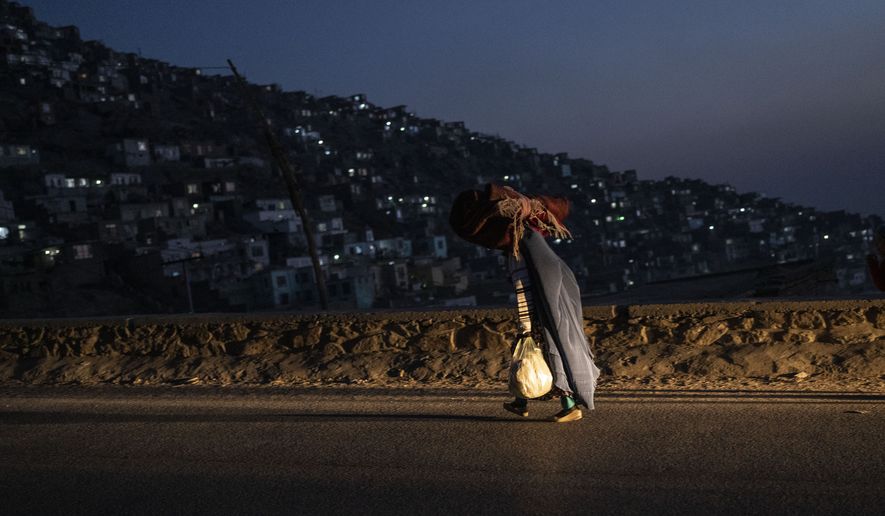 An Afghan women wearing a burka, carries a carpet as she walks in Kabul, Afghanistan, on Thursday, Dec, 2, 2021. (AP Photo/Petros Giannakouris)