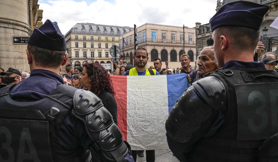 An anti heath pass demonstrator holds a French flag as he faces police officers outside the Constitutional Council in Paris, Thursday, Aug. 5, 2021. The coronavirus&#x27;s omicron variant kept a jittery world off-kilter Wednesday Dec. 1, 2021, as reports of infections linked to the mutant strain cropped up in more parts of the globe, and one official said that the wait for more information on its dangers felt like “an eternity.” (AP Photo/Michel Euler, File)