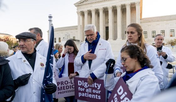 Anti-abortion healthcare workers, wearing doctors uniforms, pray together in front of the U.S. Supreme Court, Wednesday, Dec. 1, 2021, in Washington, as the court hears arguments in a case from Mississippi, where a 2018 law would ban abortions after 15 weeks of pregnancy, well before viability. (AP Photo/Andrew Harnik)