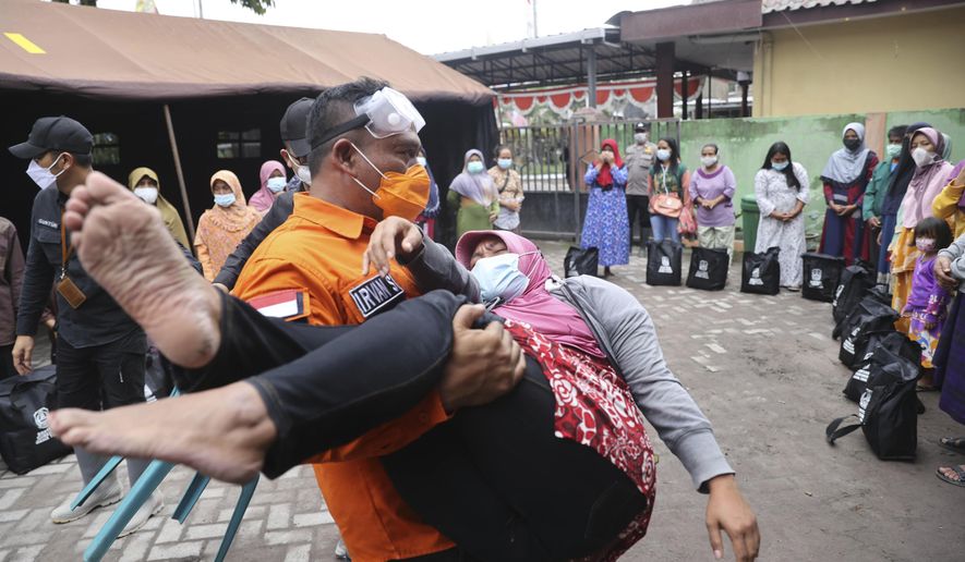 A rescuer holds a woman who fell down in a faint, after seeing her house destroyed by the eruption of Mount Semeru in Lumajang district, East Java province, Indonesia, Sunday, Dec. 5, 2021. The death toll from the eruption of the highest volcano on Indonesia&#39;s most populous island of Java has risen by a score of still missing, officials said Sunday as rain continued to lash the area and hamper the search. (AP Photo/Trisnadi)