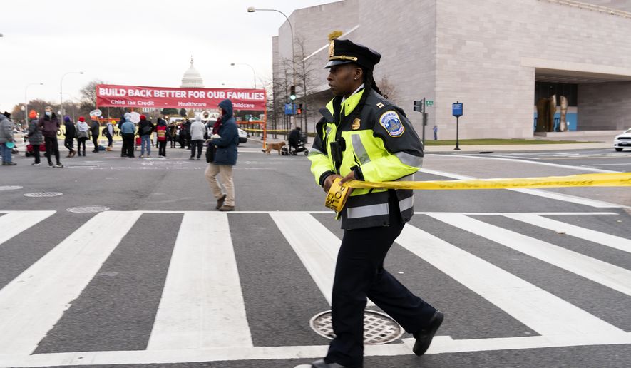 A Metropolitan Police Department officer extends yellow tape around demonstrators as they block Pennsylvania Avenue during rush hour while asking Congress to pass President Joe Biden&#39;s &quot;Build Back Better&quot; agenda, Tuesday, Dec. 7, 2021. (AP Photo/Jose Luis Magana)