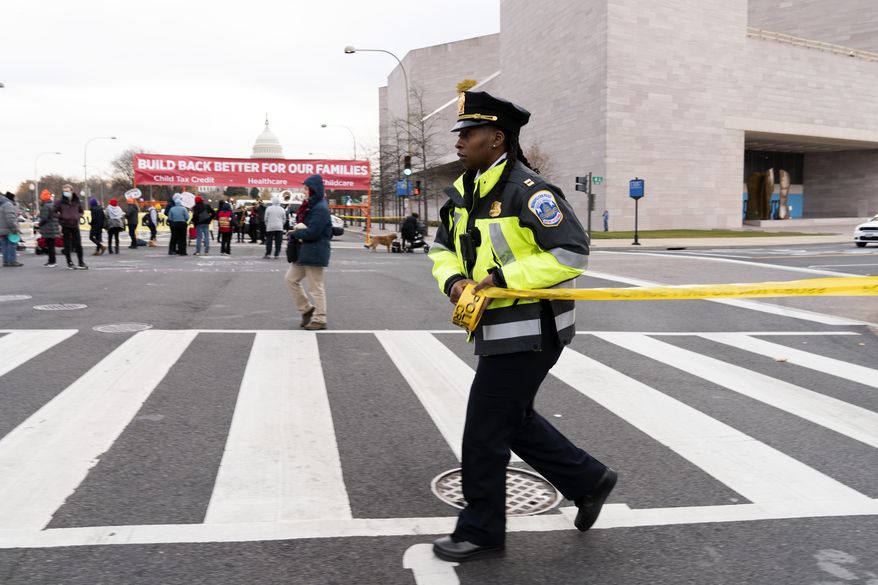 A Metropolitan Police Department officer extends yellow tape around demonstrators as they block Pennsylvania Avenue during rush hour while asking Congress to pass President Joe Biden&#39;s &quot;Build Back Better&quot; agenda, Tuesday, Dec. 7, 2021. (AP Photo/Jose Luis Magana)