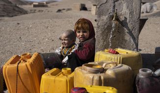 Two Afghan children sit next to a spigot as people of Kamar Kalagh village outside Herat, Afghanistan, try to fill their plastic containers with water, on Friday, Nov. 26, 2021. Afghanistan’s drought, its worst in decades, is now entering its second year, exacerbated by climate change. (AP Photo/Petros Giannakouris)