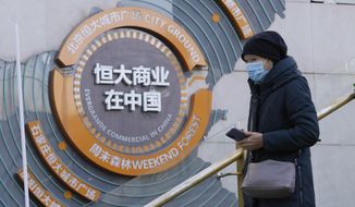 A woman passes by a display showing Evergrande&#39;s China commercial projects in Beijing, China, Tuesday, Dec. 7, 2021. Financial markets can cope with the Chinese real estate developer that is struggling to avoid defaulting on $310 billion in debt, the central bank governor said Thursday, Dec. 9, 2021, in a new effort to assure the public the economy can be shielded from fallout. (AP Photo/Ng Han Guan)
