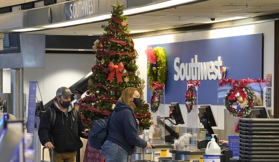 Travelers wear masks as they check in next to a holiday tree at a Southwest Airlines ticket desk, Friday, Dec. 10, 2021, at Seattle-Tacoma International Airport in Seattle. (AP Photo/Ted S. Warren)