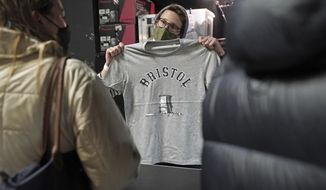 A person inside Rough Trade in Bristol, England, Saturday Dec. 11, 2021, holds up a T-shirt designed by street artist Banksy, being sold to support four people facing trial accused of criminal damage in relation to the toppling of a statue of slave trader Edward Colston. The anonymous artist posted on Instagram pictures of limited edition grey souvenir T-shirts which will go on sale on Saturday in Bristol. The shirts have a picture of Colston&#39;s empty plinth with a rope hanging off, with debris and a discarded sign nearby. (Jacob King/PA via AP)