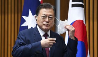 South Korean President Moon Jae-in removes his mask as he witnesses a signing ceremony at Parliament House, in Canberra, Australia, Monday, Dec. 13, 2021. Moon is on a two-day official visit to Australia. (Lukas Coch/Pool Photo via AP)