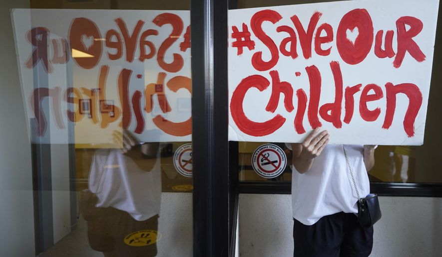 FILE - An anti-vaccine mandate protester holds a sign outside the front windows of the Los Angeles Unified School District headquarters in Los Angeles, Sept. 9, 2021. The Los Angeles school district is voting on a proposal to delay its Jan. 10 student COVID-19 vaccine mandate until the fall of 2022, faced with thousands of students 12 and older who are not fully vaccinated and would be barred from in-person classes. (AP Photo/Damian Dovarganes, File)