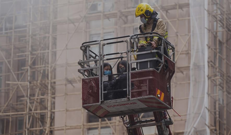 Two women are rescued by a firefighter in a bucket crane outside the World Trade Centre located in the city&#39;s popular Causeway Bay shopping district of Hong Kong, Wednesday, Dec. 15, 2021. Dozens of people were trapped on the rooftop of the Hong Kong skyscraper after a major fire broke out Wednesday, as firefighters rushed to rescue them and put out the blaze. (AP Photo)