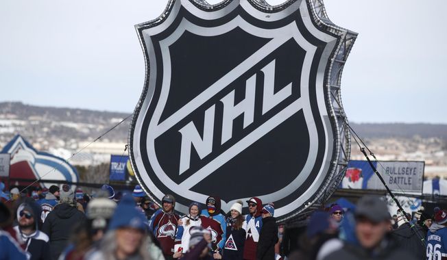 FILE - In this Feb. 15, 2020, file photo, fans pose below the NHL league logo at a display outside Falcon Stadium before an NHL Stadium Series outdoor hockey game between the Los Angeles Kings and Colorado Avalanche, at Air Force Academy, Colo. (AP Photo/David Zalubowski, File)