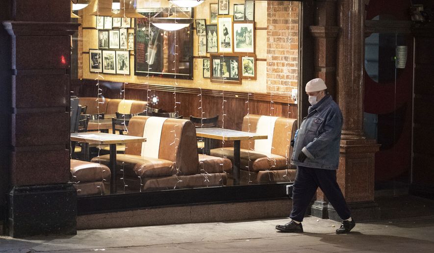 A pedestrian wearing a mask walks past an empty restaurant in central London on Tuesday Dec. 21, 2021. British Prime Minister Boris Johnson said on Monday that his government reserves the "possibility of taking further action" to protect public health as Omicron spreads across the country. (Dominic Lipinski/PA via AP)