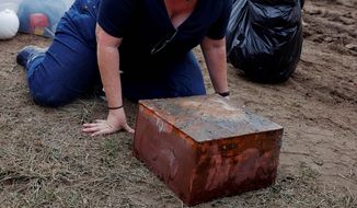 Katherine Ridgway, state archaeological conservator, prepares to wrap and remove a box believed to be the 1887 time capsule that was put under Confederate Gen. Robert E. Lee statue&#39;s pedestal Monday, Dec. 27, 2021, in Richmond, Va. In back, Everett Mercer, 10, son of Governor Ralph Northam&#39;s chief staff Clark Mercer, stands by to help. Crews wrapping up the removal Monday of the giant pedestal that once held a statue of Gen. Lee found what appeared to be a second and long-sought-after time capsule, Virginia Gov. Ralph Northam said.  (Eva Russo/Richmond Times-Dispatch via AP)