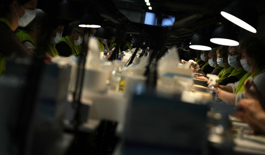 Pharmacists fill syringes from vials of the Moderna booster vaccine at the Antwerp Expo vaccine center in Antwerp, Belgium on Monday, Dec. 27, 2021. In Belgium, many flocked to their local vaccine center to receive their booster shots and stay ahead of the surging omicron infections. Others faced their first real test of the latest COVID-19 measures on Monday, with shopping reduced to a maximum of two along with closures of movie theaters and concert halls. (AP Photo/Virginia Mayo)
