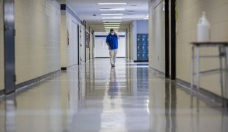 A middle school principal walks the empty halls of his school as he speaks with one of his teachers to get an update on her COVID-19 symptoms, Friday, Aug., 20, 2021, in Wrightsville, Ga. On Monday, Dec. 27, 2021, U.S. health officials cut isolation restrictions for Americans who catch the coronavirus from 10 to five days, and also shortened the time that close contacts need to quarantine. (AP Photo/Stephen B. Morton, File)