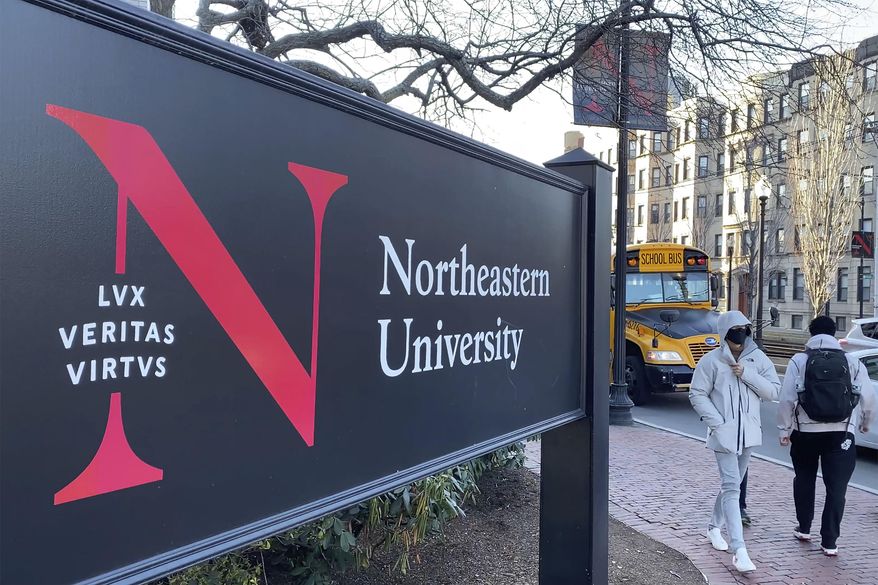 Pedestrians walk near a Northeastern University sign on the school's campus in Boston, Jan. 31, 2019. At Northeastern University in Boston, one of a growing number of schools requiring boosters, students are returning to campus as planned.(AP Photo/Rodrique Ngowi, File)