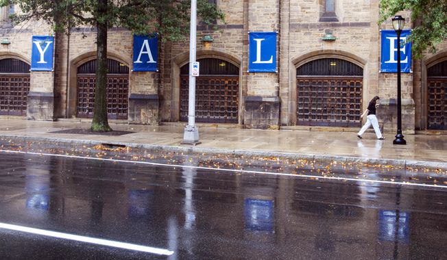 A woman walks by a Yale sign reflected in the rainwater in the street on the Yale University campus in New Haven, CT, Aug. 22, 2021. (AP Photo/Ted Shaffrey, File)