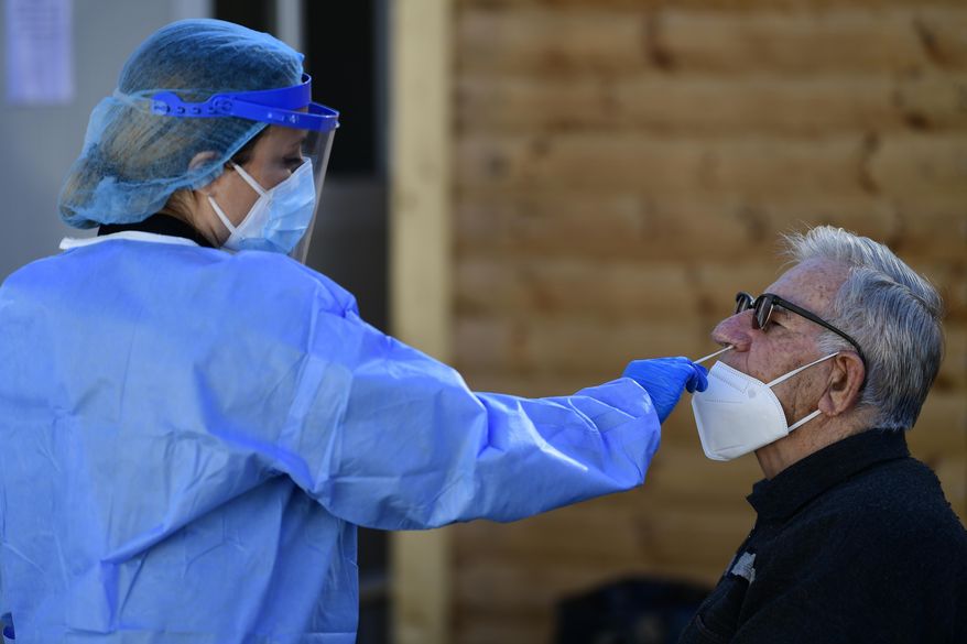 A medical staff conducts a COVID-19 rapid test on a man in Athens, Greece, Tuesday, Jan. 4, 2022. A vaccination mandates for country residents over 60 goes into effect later this month as a surge in infections driven by the omicron variant of COVID-19 continues. Authorities will decide later today whether to reopen schools on schedule on Jan. 10. (AP Photo/Michael Varaklas)