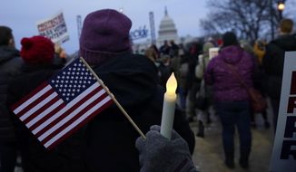 With the U.S. Capitol building in the background, a person holds an American flag and a flameless candle during a vigil Thursday, Jan. 6, 2022, in Washington, on the one year anniversary of the attack on the U.S. Capitol. (AP Photo/Julio Cortez)