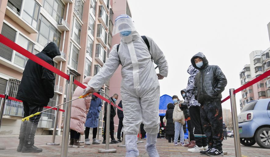A worker wearing a protection suit sprays disinfectant as residents wearing face masks to protect from the coronavirus line up for the coronavirus test during a mass testing in north China&#39;s Tianjin municipality, Sunday, Jan. 9, 2022. Tianjin, a major Chinese port city near the capital Beijing, began mass testing of its 14 million residents on Sunday, after a cluster of a dozen of children and adults tested positive for COVID-19, including a few with the omicron variant. (Chinatopix Via AP)