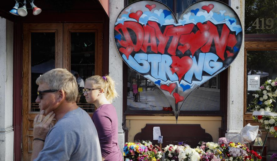 In this Aug. 7, 2019 file photo, passers-by walk past a makeshift memorial for the slain and injured victims of a mass shooting that occurred in the Oregon District in Dayton, Ohio. Newly released Dayton police records say all of the people killed outside a strip of nightclubs appear to have been shot at random. The FBI finished its investigation late last year without determining whether accused shooter Connor Betts intentionally shot his sister. (AP Photo/John Minchillo, File)