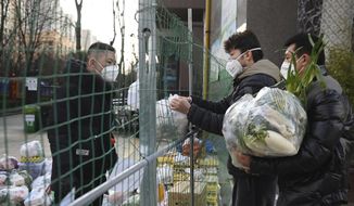 In this photo released by Xinhua News Agency, a volunteer at left receives daily necessities on behalf of residents under home quarantine at the fence to a community in Yanta District of Xi&#39;an, capital of northwest China&#39;s Shaanxi Province, Jan. 12, 2022. (Tao Ming/Xinhua via AP, File)