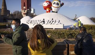 People wearing face masks to help protect against the coronavirus look at a display of the Winter Paralympic mascot Shuey Rhon Rhon, left, and Winter Olympic mascot Bing Dwen Dwen near the Olympic Green in Beijing, Wednesday, Jan. 12, 2022. Just weeks before hosting the Beijing Winter Olympics, China is battling multiple coronavirus outbreaks in half a dozen cities, with the one closest to the capital driven by the highly transmissible omicron variant. (AP Photo/Mark Schiefelbein)