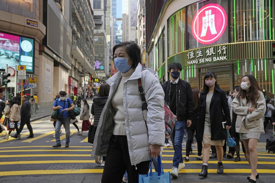 People walk across a street in Hong Kong, Tuesday, Jan. 11, 2022. In an effort to limit omicron outbreaks, Hong Kong is closing kindergartens and primary schools after infections were reported in students, city leader Carrie Lam said Tuesday. Schools are to close by Friday and remain shut until at least the Lunar New Year holiday in the first week of February. (AP Photo/Kin Cheung)