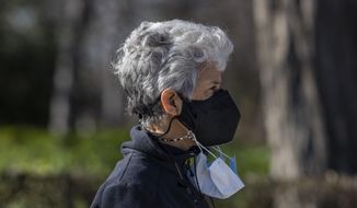A woman wearing multiple face masks walks in the Retiro park in Madrid, Spain, Wednesday, Jan. 12, 2022. Italy, Spain and other European countries are re-instating or stiffening mask mandates as their hospitals struggle with mounting numbers of COVID-19 patients. (AP Photo/Bernat Armangue) ** FILE **