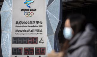A woman wearing a face mask to protect against COVID-19 walks past a clock counting down the time until the opening ceremony of the 2022 Winter Olympics in Beijing, Saturday, Jan. 15, 2022. China announced Monday that members of the Chinese public no longer will be able to buy tickets to the Beijing Winter Olympic as organizers struggle to contain the latest coronavirus outbreak, with the games just three weeks away. (AP Photo/Mark Schiefelbein)