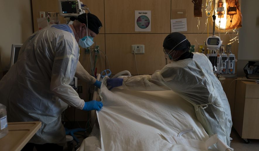 Respiratory therapist Frans Oudenaar, left, and registered nurse Bryan Hofilena cover a body of a COVID-19 patient with a sheet at Providence Holy Cross Medical Center in Los Angeles, Dec. 14, 2021. The fast-moving omicron variant may cause less severe disease on average, but COVID-19 deaths in the U.S. are climbing and modelers forecast 50,000 to 300,000 more Americans could die by the time the wave subsides in mid-March. (AP Photo/Jae C. Hong, File)